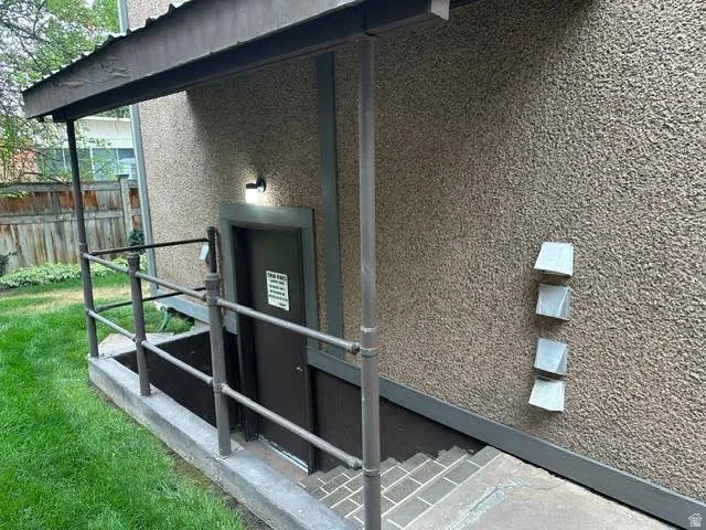 Stucco exterior with a covered entry, metal handrails, exterior lighting, and a fenced perimeter
