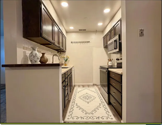 Galley kitchen featuring wood-finish flooring, recessed lighting, and dark wood cabinetry