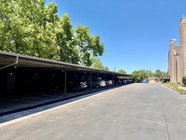 Covered parking structure with multiple bays of which each unit has a private space, featuring a paved driving surface, and mature trees overhead