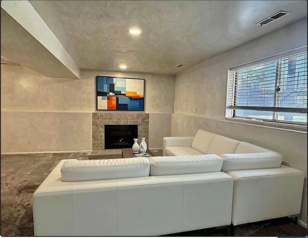 Living room featuring a tiled fireplace with a dark insert, a large window with natural light, recessed ceiling lighting, and a visible ceiling beam