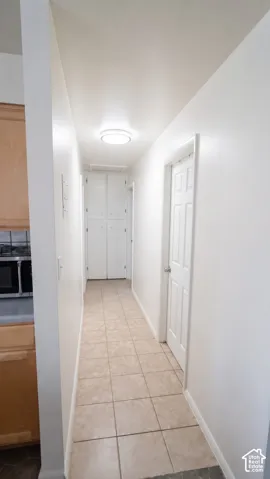 Hallway featuring neutral ceramic tile flooring, built-in floor-to-ceiling storage cabinetry, a six-panel interior door, and a flush-mount circular ceiling light fixture