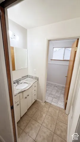 Vanity featuring a stone-patterned countertop, an oval undermount sink, white cabinetry with integrated storage drawers, and ceramic tile flooring