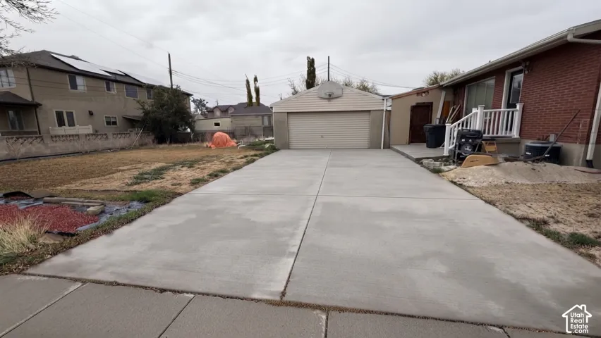 Concrete driveway leading to a detached two-car garage with white vinyl siding and a red brick exterior on the main structure