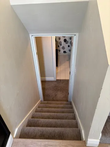 Carpeted staircase with white trim leading to a lower level with additional carpeted flooring and a visible bathroom entrance featuring white tile