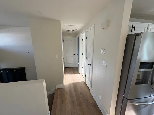 Hallway featuring wood-finish flooring, white paneled doors with black hardware, and a modern thermostat