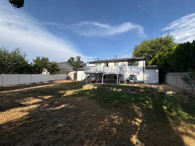 Expansive backyard featuring a multi-level deck, white vinyl fencing, a detached storage shed, and mature perimeter trees