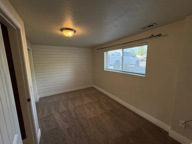 Room featuring a prominent shiplap accent wall, patterned carpet flooring, and a window with blinds