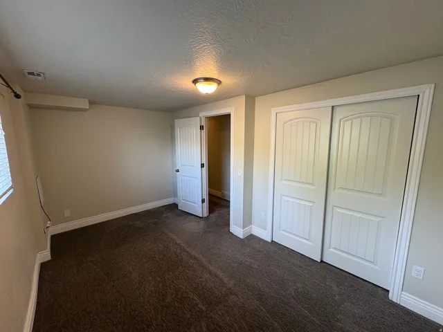Carpeted room featuring a ceiling-mounted light fixture, white trim, and a window with blinds