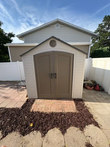 Exterior storage shed with double doors, complemented by a brick paver pathway and surrounding wood mulch