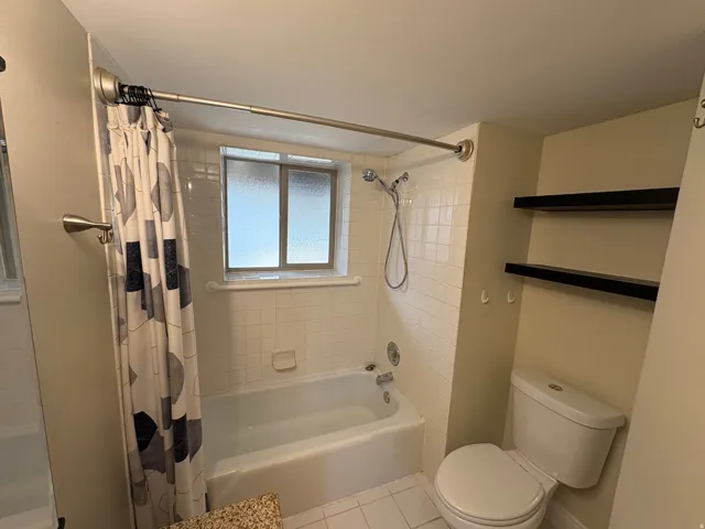 Full bathroom featuring a tub-shower combination with white tile surround, frosted window, and a white toilet
