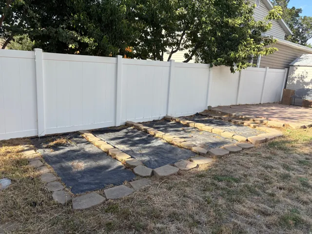 Private backyard featuring a white vinyl fence, three raised garden beds with stone edging, and a brick paver patio area