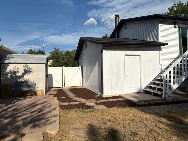 Exterior storage shed with a shingled roof, white double-gate access, dedicated exterior access, a paved patio area, and a stepped entry