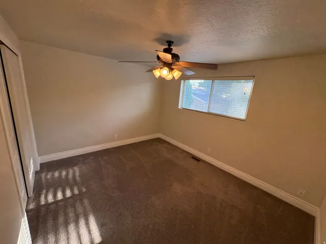 Carpeted room with a ceiling fan light fixture, white baseboards, and a window with blinds