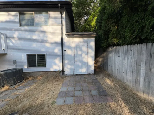 Rear exterior featuring white horizontal siding, a built-in storage shed with a panel door, and a paver patio area