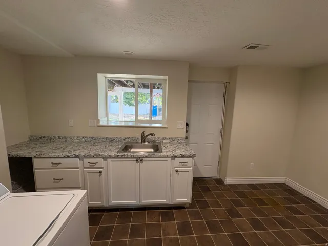 Utility room featuring a stainless steel sink, patterned countertop, white cabinetry with silver hardware, and tile flooring