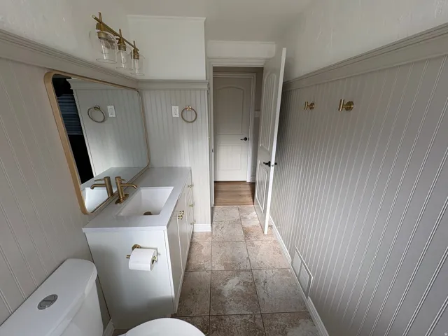 Bathroom featuring a white vanity with an integrated sink, gold-tone hardware, and a framed mirror