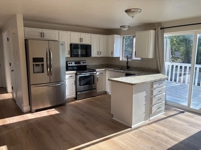 Modern kitchen featuring stainless steel appliances, white cabinetry, granite countertops, and wood-finish flooring
