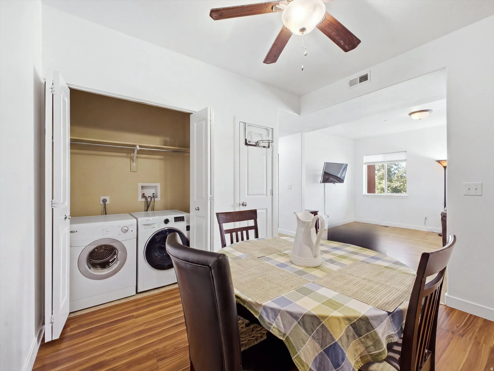 In-unit laundry with washer and dryer included, wood-finish flooring, white walls, and a recessed ceiling fan with integrated lighting