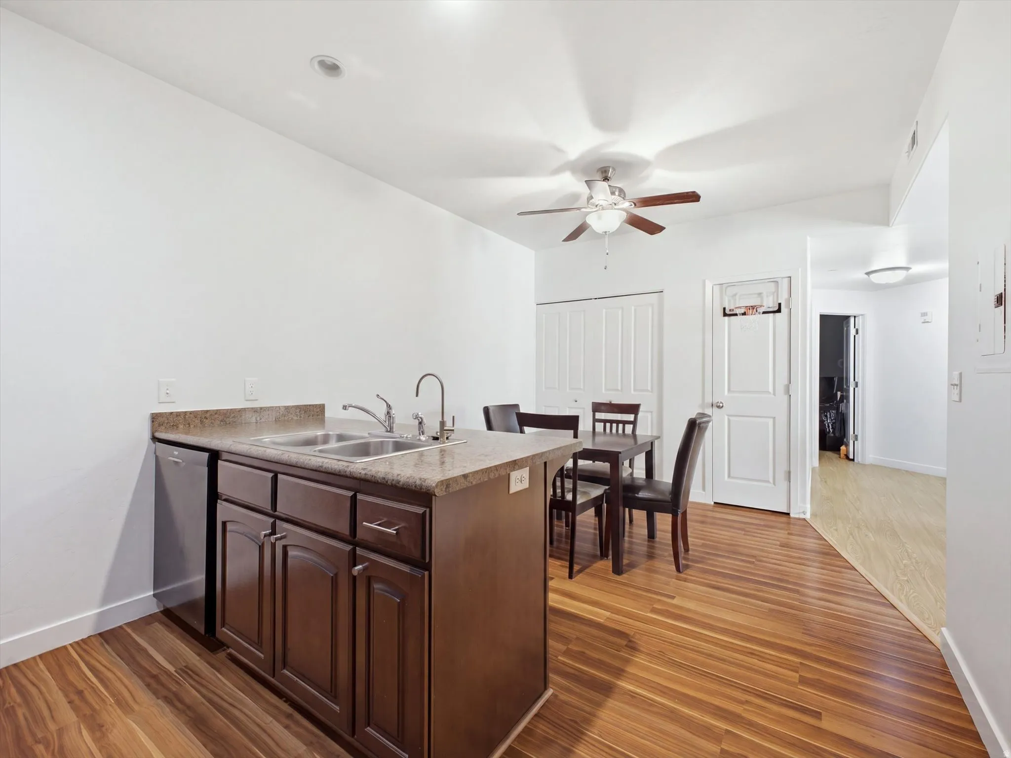 Open-concept kitchen featuring a wood-finish island with prep space and storage, stainless steel sink with gooseneck faucet, wood-finish flooring throughout, ceiling fan with integrated lighting, and white cabinetry with paneled doors