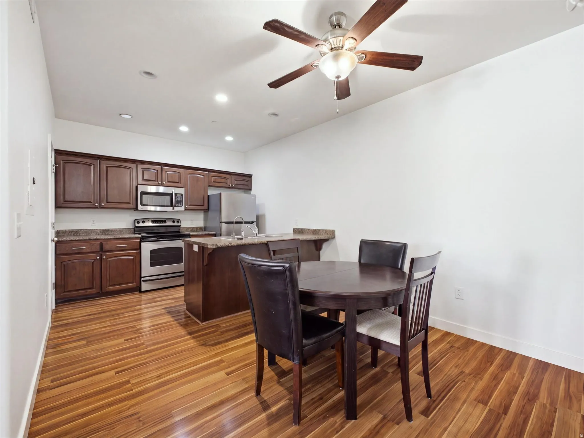 Hardwood flooring, dark wood cabinetry, stainless steel appliances, recessed lighting, and a ceiling fan with light fixture