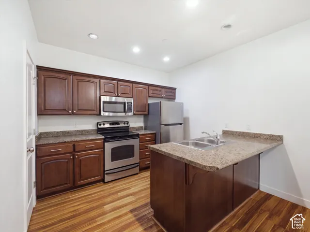 Wood-finish flooring, dark wood cabinetry, stainless steel appliances, granite-style countertops, and recessed lighting