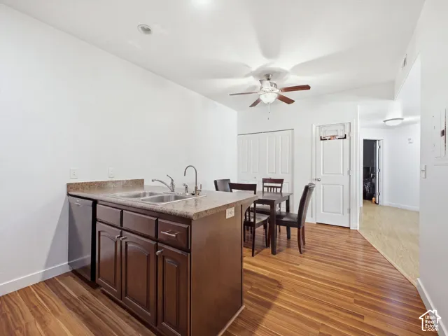 Open-concept kitchen featuring a wood-finish island with prep space and storage, stainless steel sink with gooseneck faucet, wood-finish flooring throughout, ceiling fan with integrated lighting, and white cabinetry with paneled doors