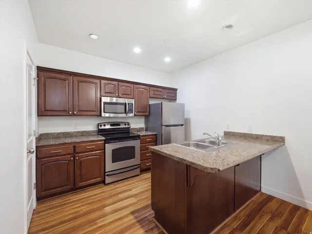 Wood-finish flooring, dark wood cabinetry, stainless steel appliances, granite-style countertops, and recessed lighting