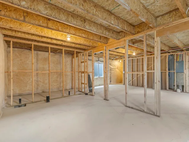Unfinished basement featuring wood framing, exposed ceiling joists, concrete flooring, and an egress window