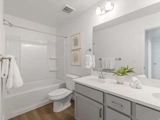 Bathroom featuring a dual-sink vanity with light gray cabinetry and a light-toned countertop, a full-width mirror, and a shower-over-tub combination with a white surround