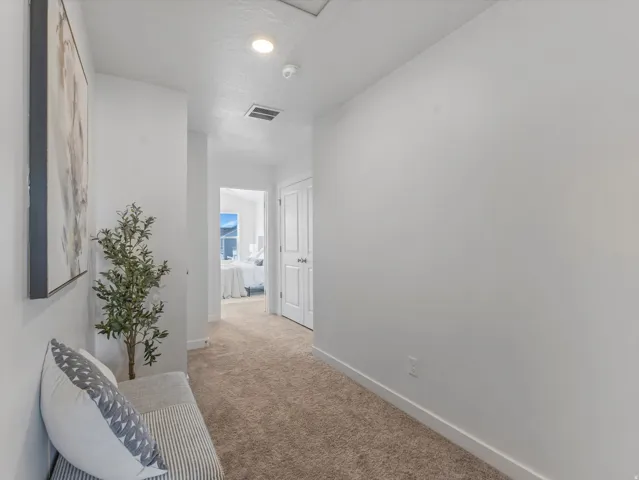 Hallway with tan carpet flooring, white baseboards, and recessed lighting