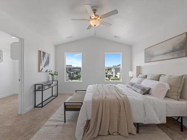 Vaulted ceiling bedroom featuring a ceiling fan with integrated lighting, two rectangular windows, and neutral carpeting