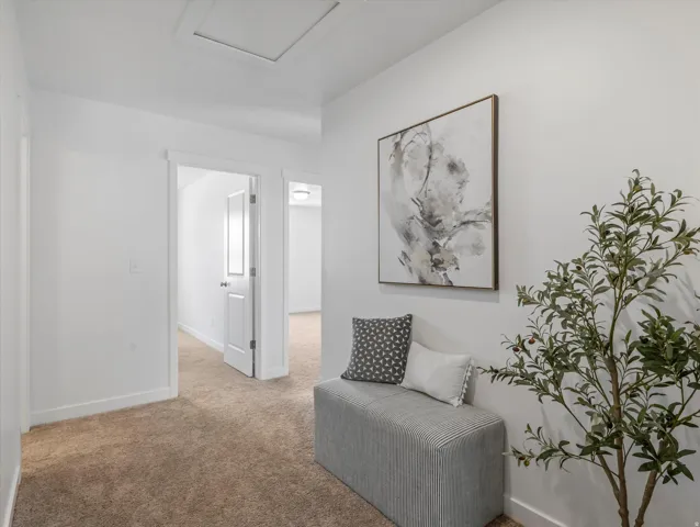 Carpeted hallway featuring bright white walls, white trim, and a white ceiling with an attic access panel