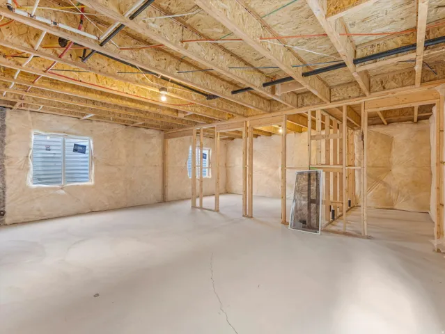 Unfinished basement offering substantial customization potential, featuring open wood framing, exposed joists, perimeter insulation, concrete flooring, and multiple window openings