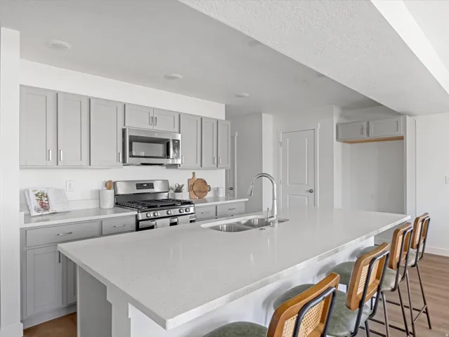Modern kitchen featuring light gray cabinetry, stainless steel appliances, a double basin sink, and an expansive island with seating