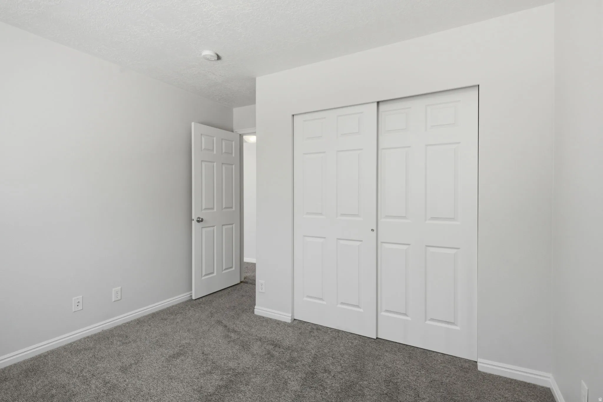 Carpeted room featuring a white six-panel interior door, white baseboards, and a bi-fold closet door