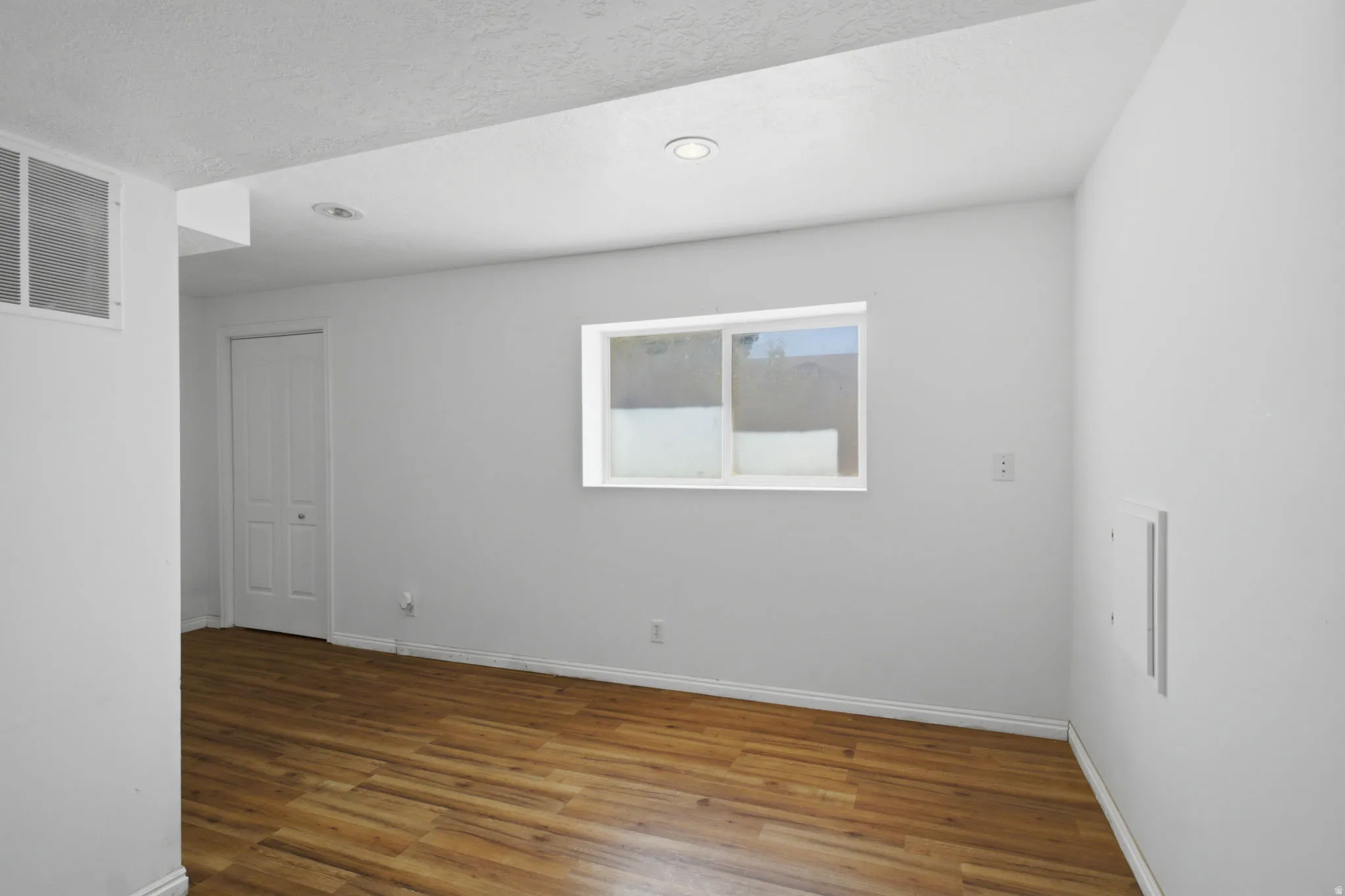 Room featuring wood-finish flooring, recessed lighting, and a white-framed window