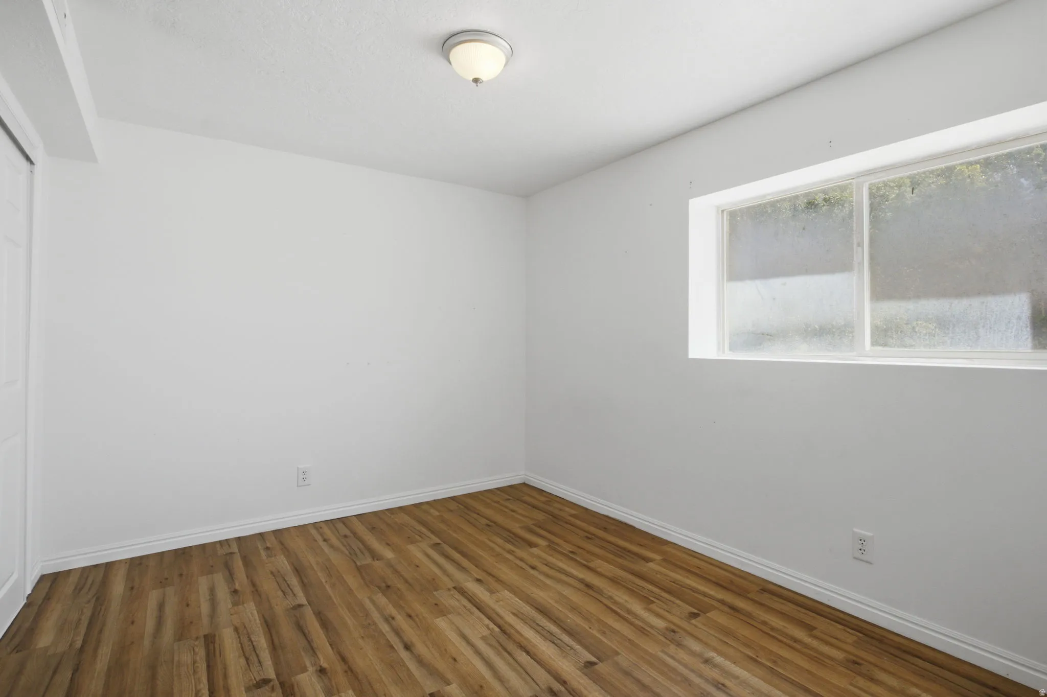 Room featuring wood-finish flooring, white baseboards, a single window, and a flush mount ceiling light fixture