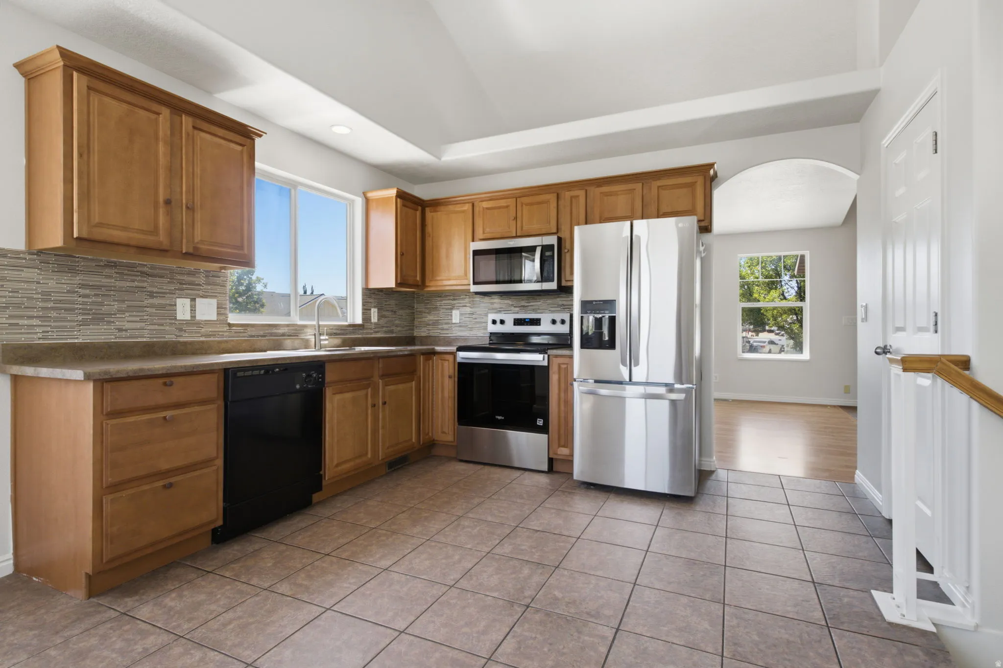Kitchen featuring wood cabinetry, stainless steel appliances, mosaic tile backsplash, and a large window above the sink