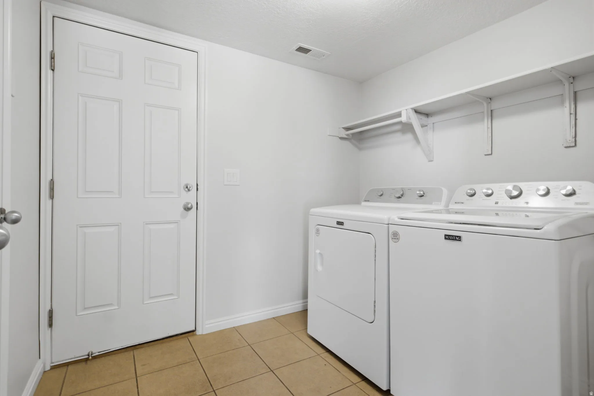 Dedicated laundry area featuring ceramic tile flooring, neutral wall paint, and a built-in white shelving unit with a hanging rod