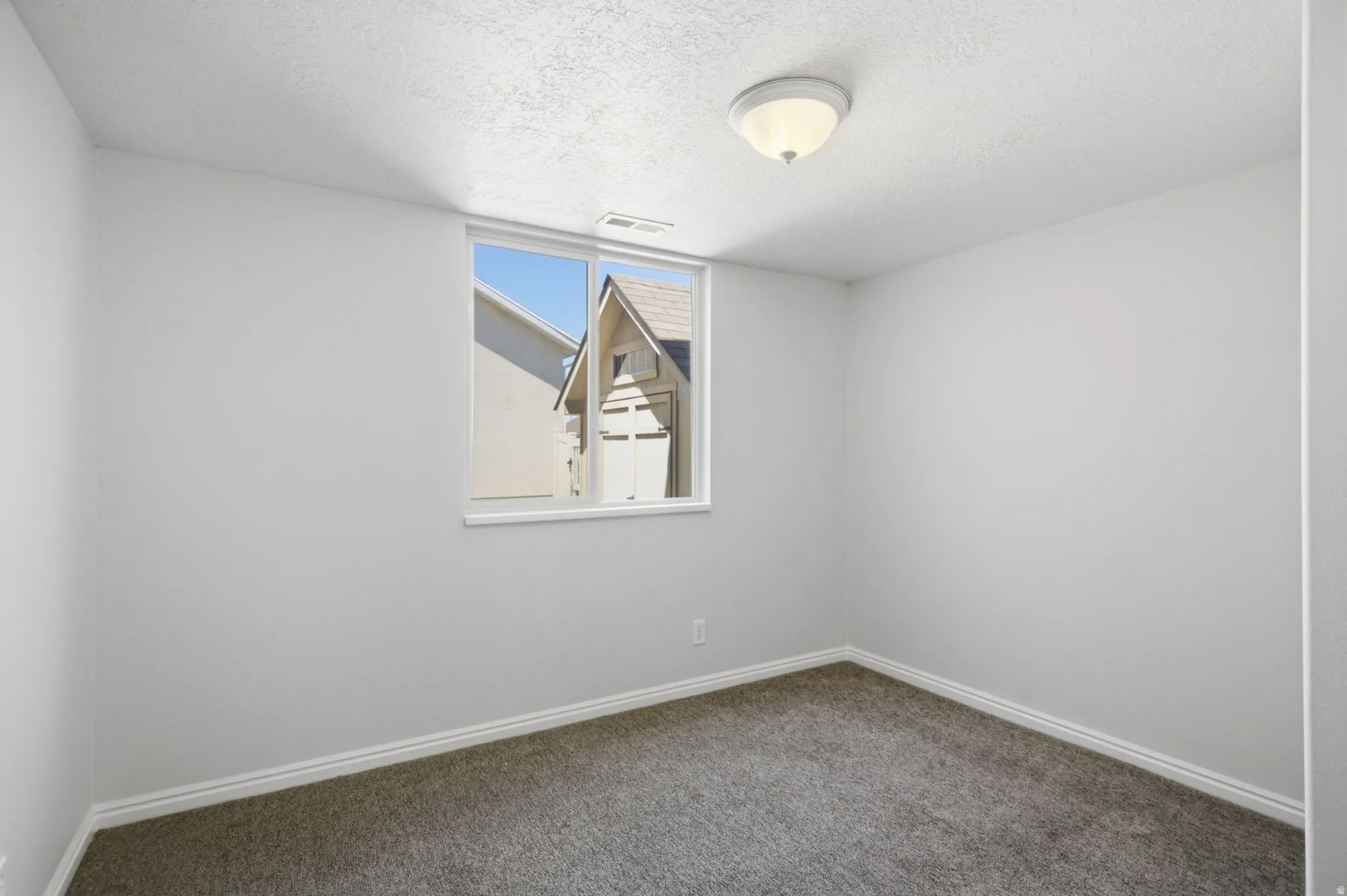 Neutral wall color, window with white trim, white baseboards, textured ceiling, and flush-mount ceiling light