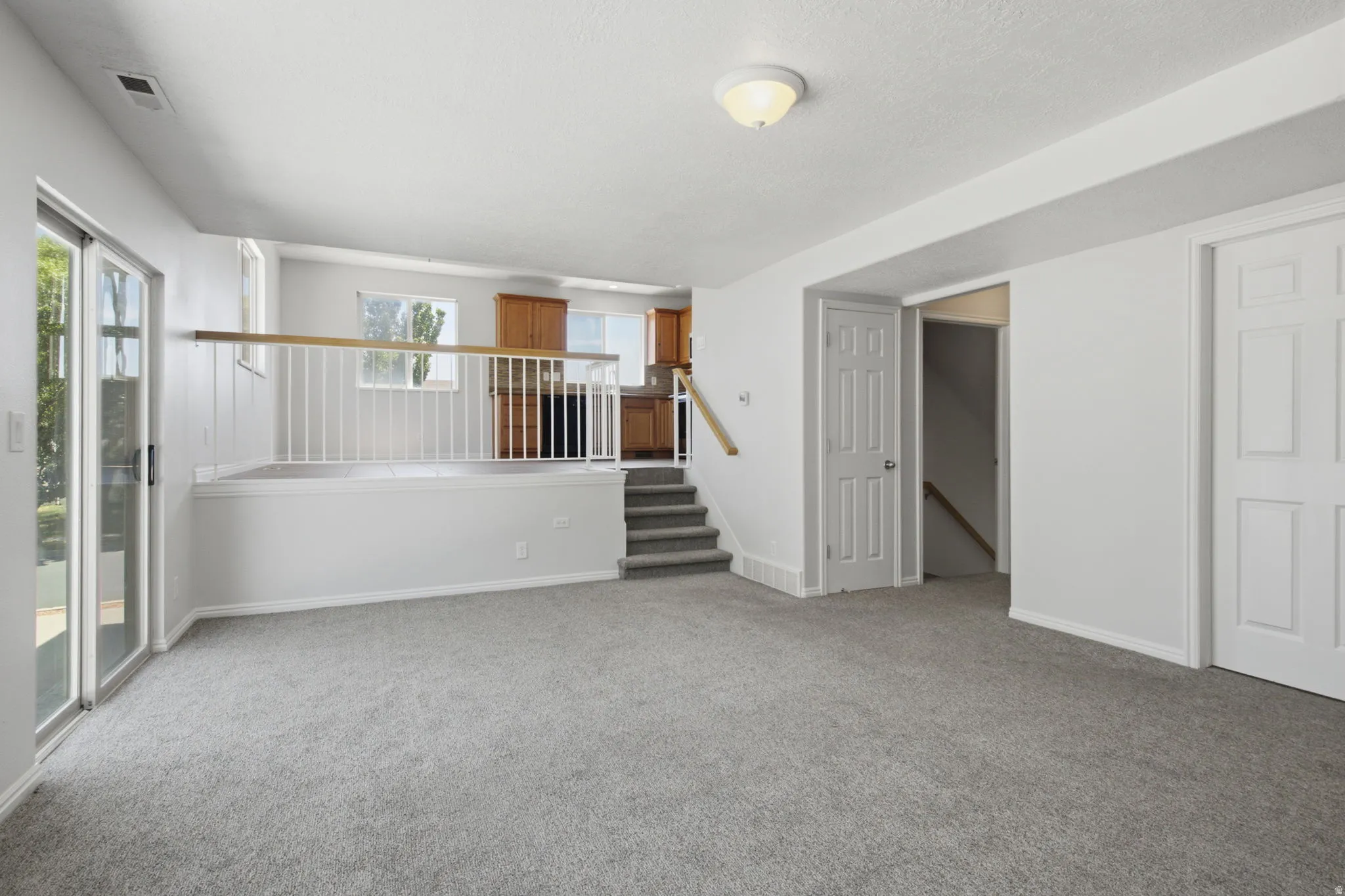 Open-concept living area featuring light gray carpet, white walls, and a sliding glass door