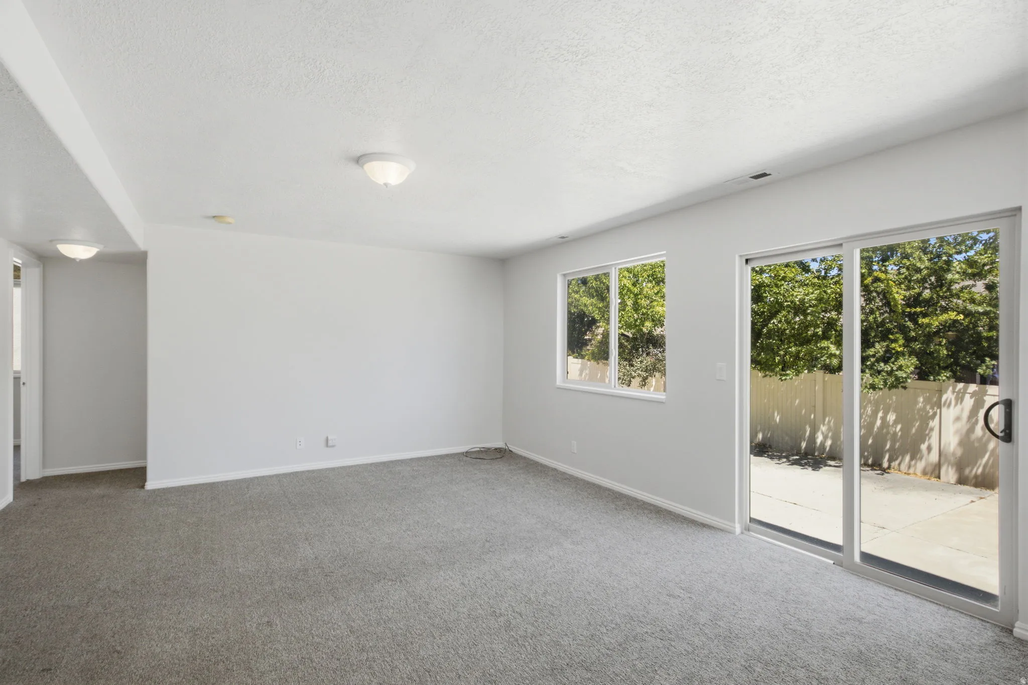 Spacious room featuring neutral carpeting, a large window, and a glass sliding door