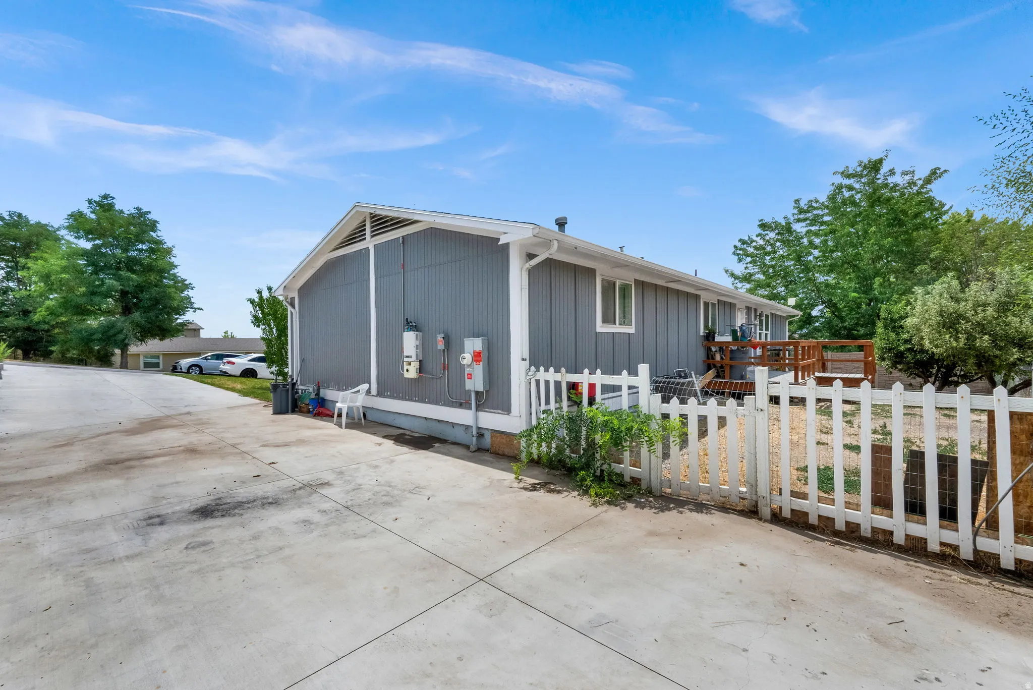 Side exterior featuring gray siding, a white picket fence, a wooden deck, and a concrete driveway