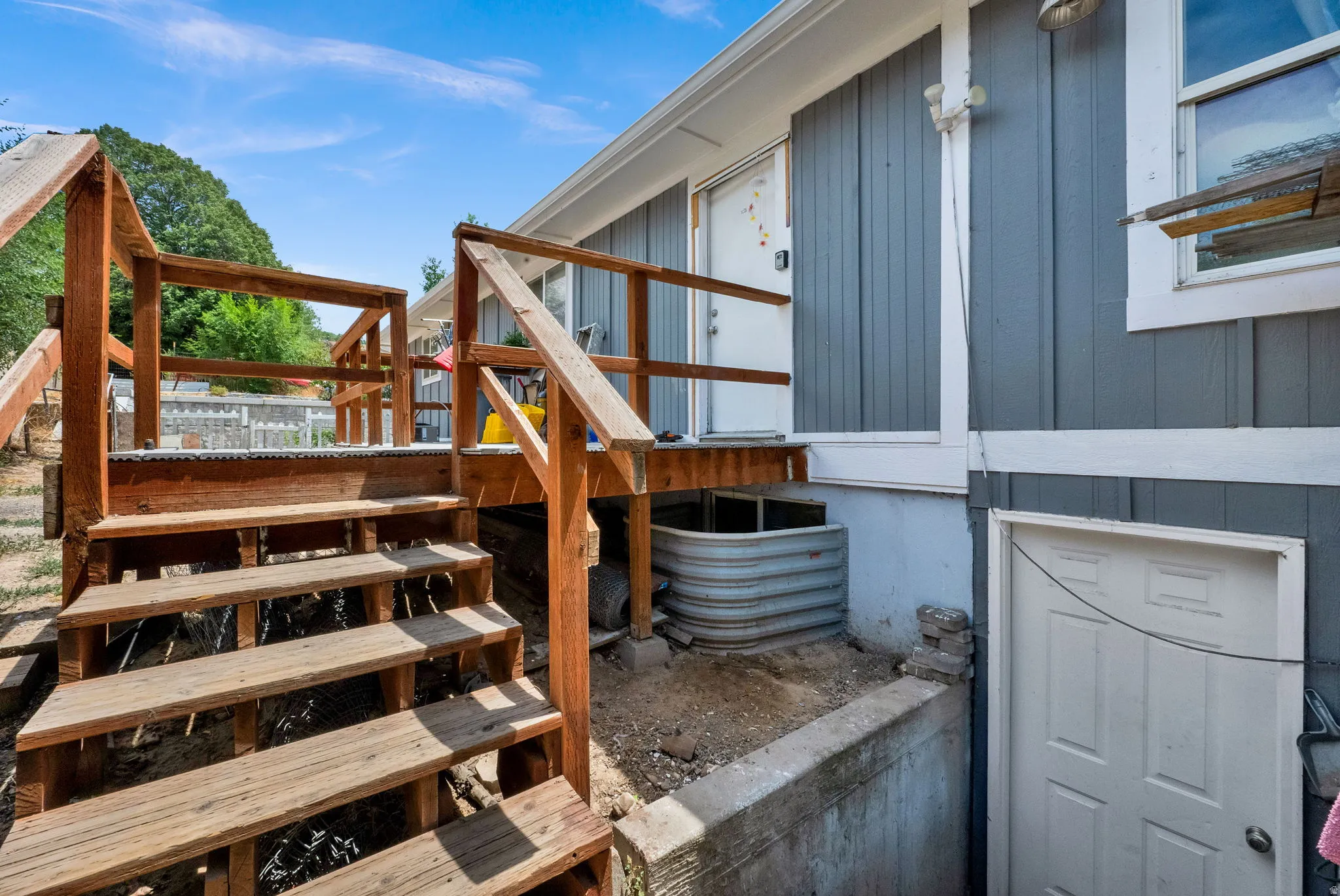 Wood deck with multiple steps and railings, featuring a window well and two exterior doors