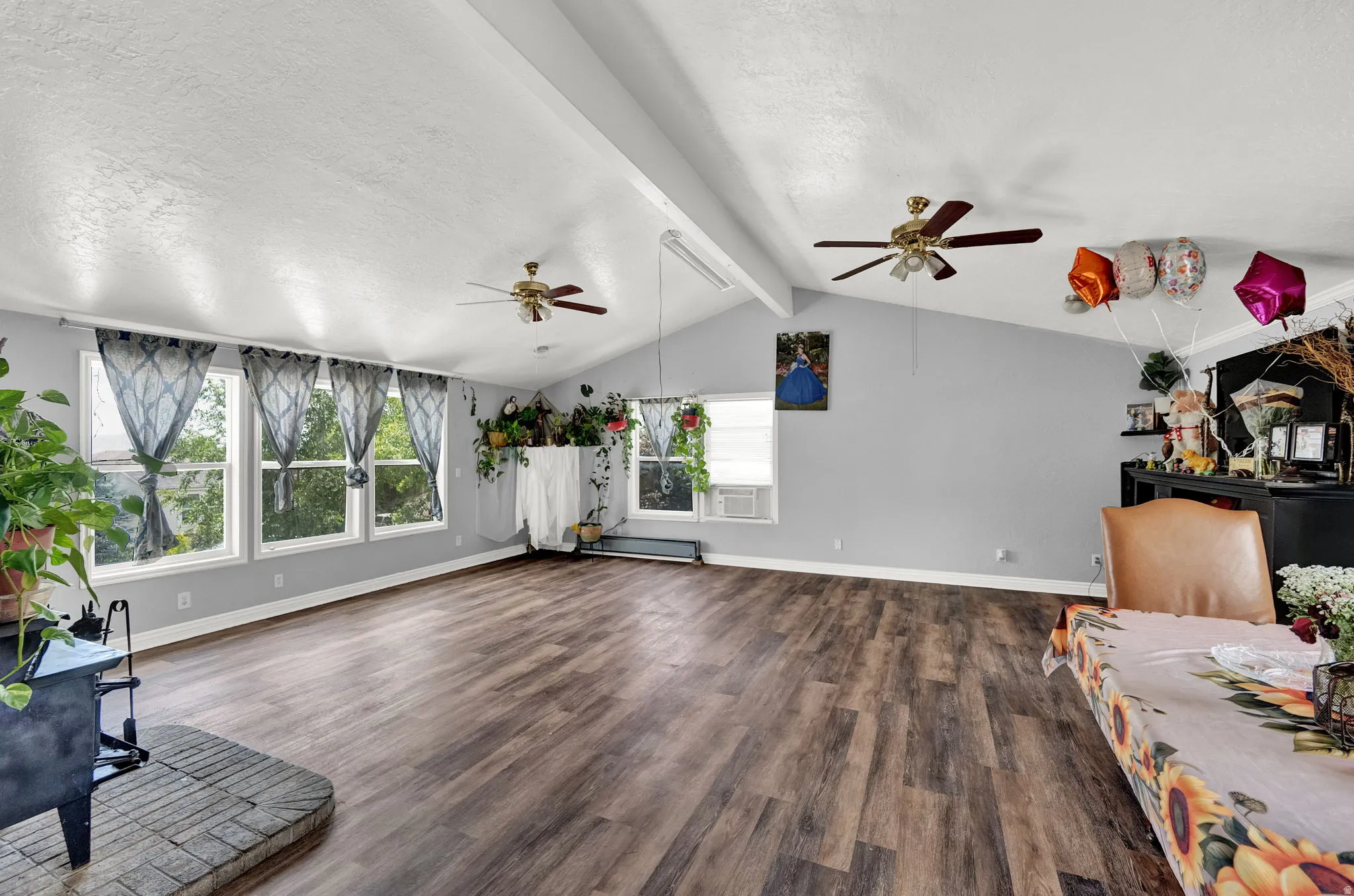 Spacious room featuring vaulted ceilings, wood-finish flooring, and multiple windows