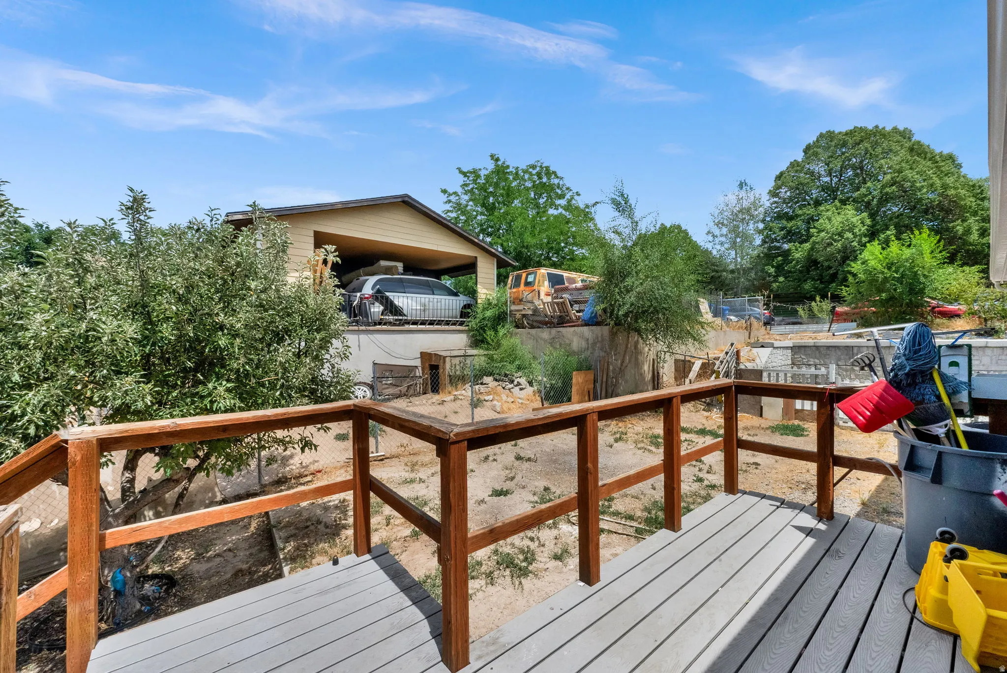 Outdoor deck with composite flooring and wood railing, offering a partial view of a detached carport structure