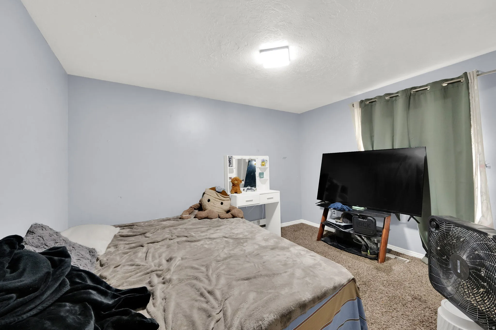 Bedroom featuring light blue walls, a window with curtains, a ceiling-mounted light fixture, and carpet flooring