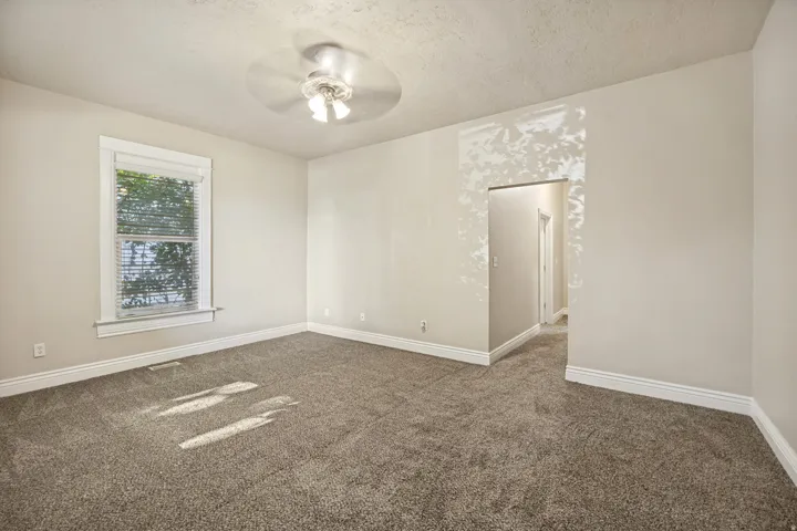 Spacious room featuring neutral carpeting, a ceiling fan with integrated lighting, a single window with blinds, and white baseboards