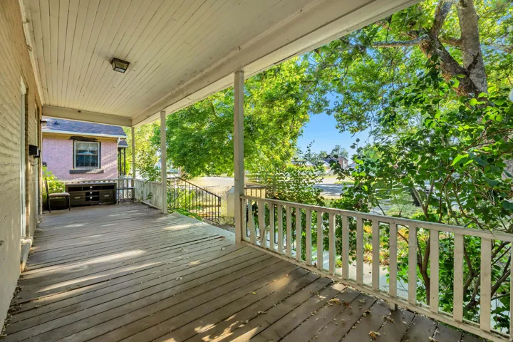 Expansive front porch featuring wood plank flooring, a white spindle railing, and a beadboard ceiling with an attached light fixture