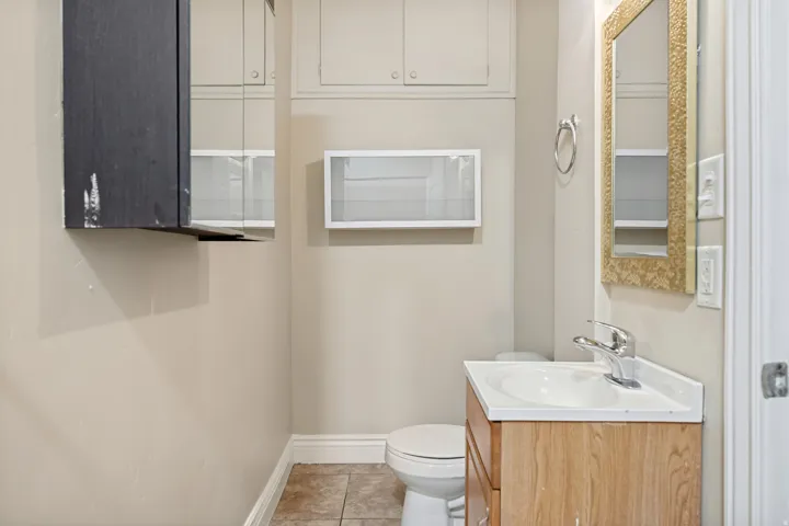 Bathroom featuring a wood-finish vanity with an integrated sink, a gold-framed mirror, and a white toilet